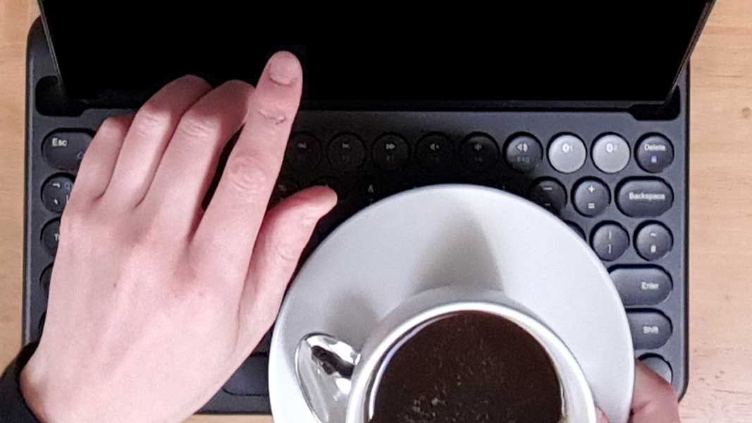 Photograph of a tablet computer and attached keyboard resting on a wooden table while a person points at the screen.